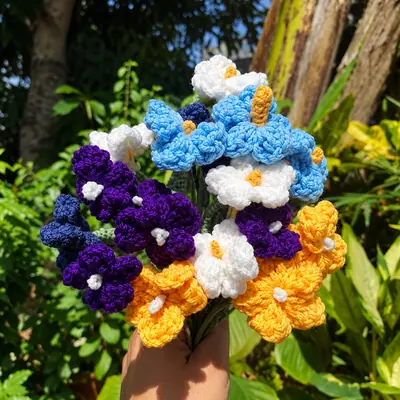 A bunch of crocheted flowers in blue, purple, orange and cream on green crocheted leafy stems.