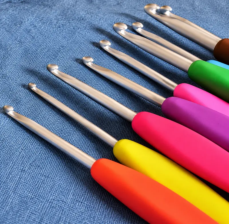 Crochet hooks with colourful soft handles in pink, red, green and blue, fanned out on blue fabric to show their sizes.