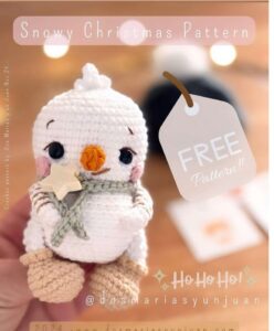 White crocheted snowman with a carrot nose, green scarf and wooden star, photographed on a warm festive background.